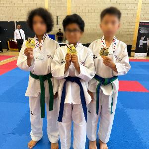 Three students holding gold medals from the London Taekwondo Interclub